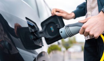Man opening car's charge socket and holding charger at charge station