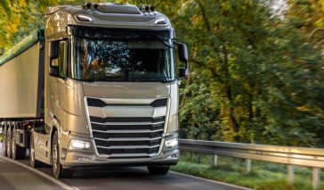 Powerful gray tractor with semitrailer driving along an empty road through green forest. Dynamic long haul mood with golden hour light and reliable logistics vibe.